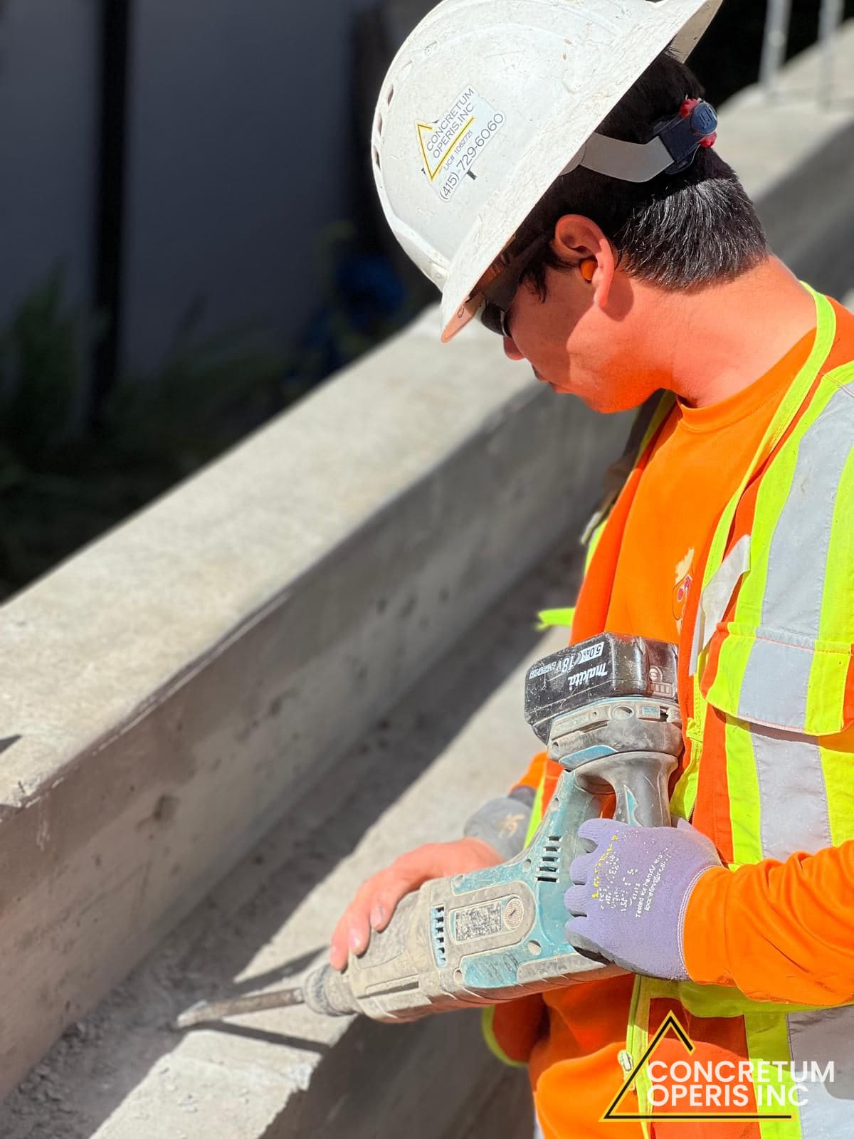 Worker using a power chisel to finish the edge of a poured concrete wall cap