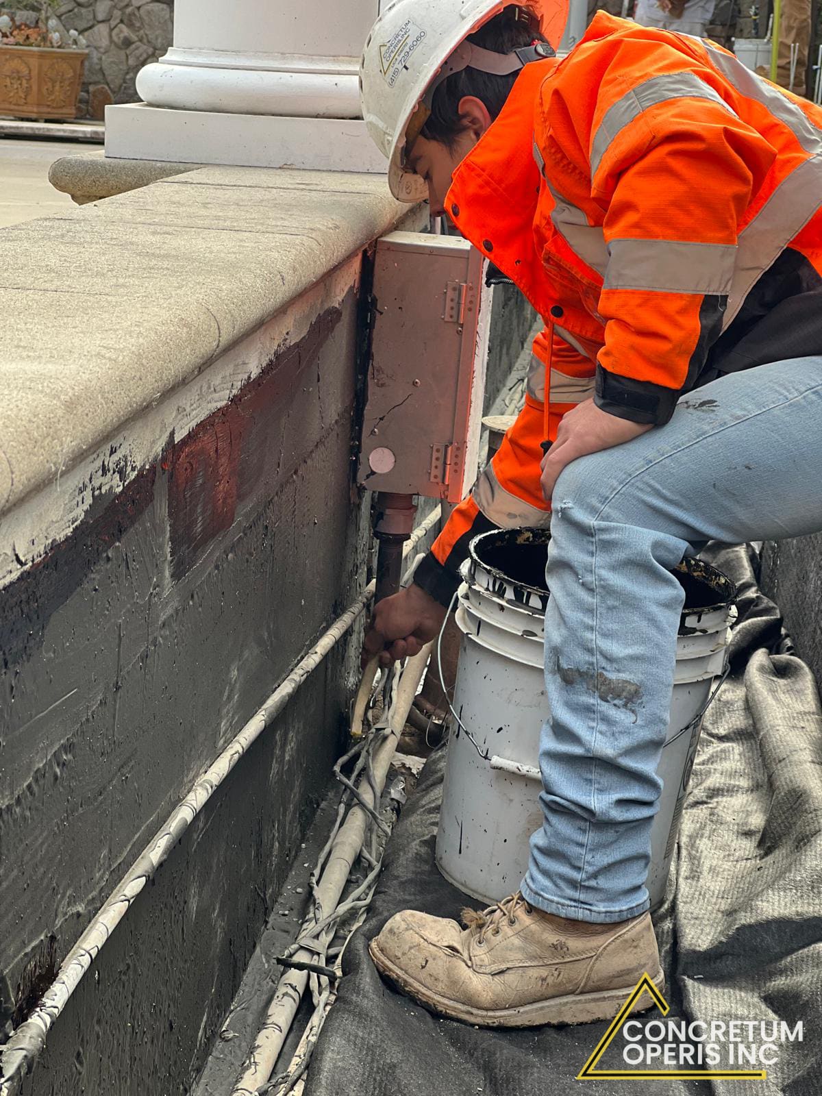 Crew member applying waterproofing tar along the foundation wall base in Richmond, CA