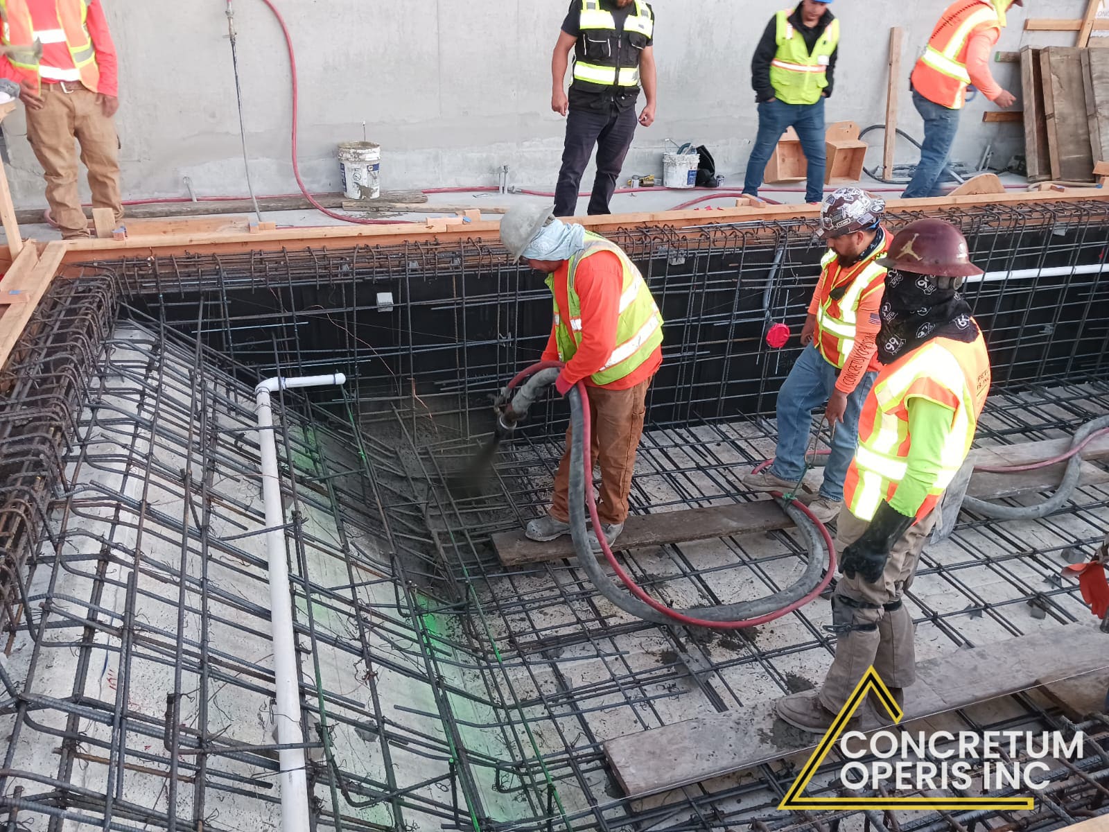 Crew pumping concrete into a rebar-formed rooftop planter box high above the city