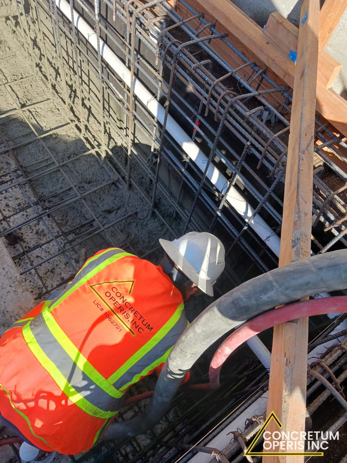 Concretum Operis crew member guiding a concrete pump hose into rebar formwork on a rooftop