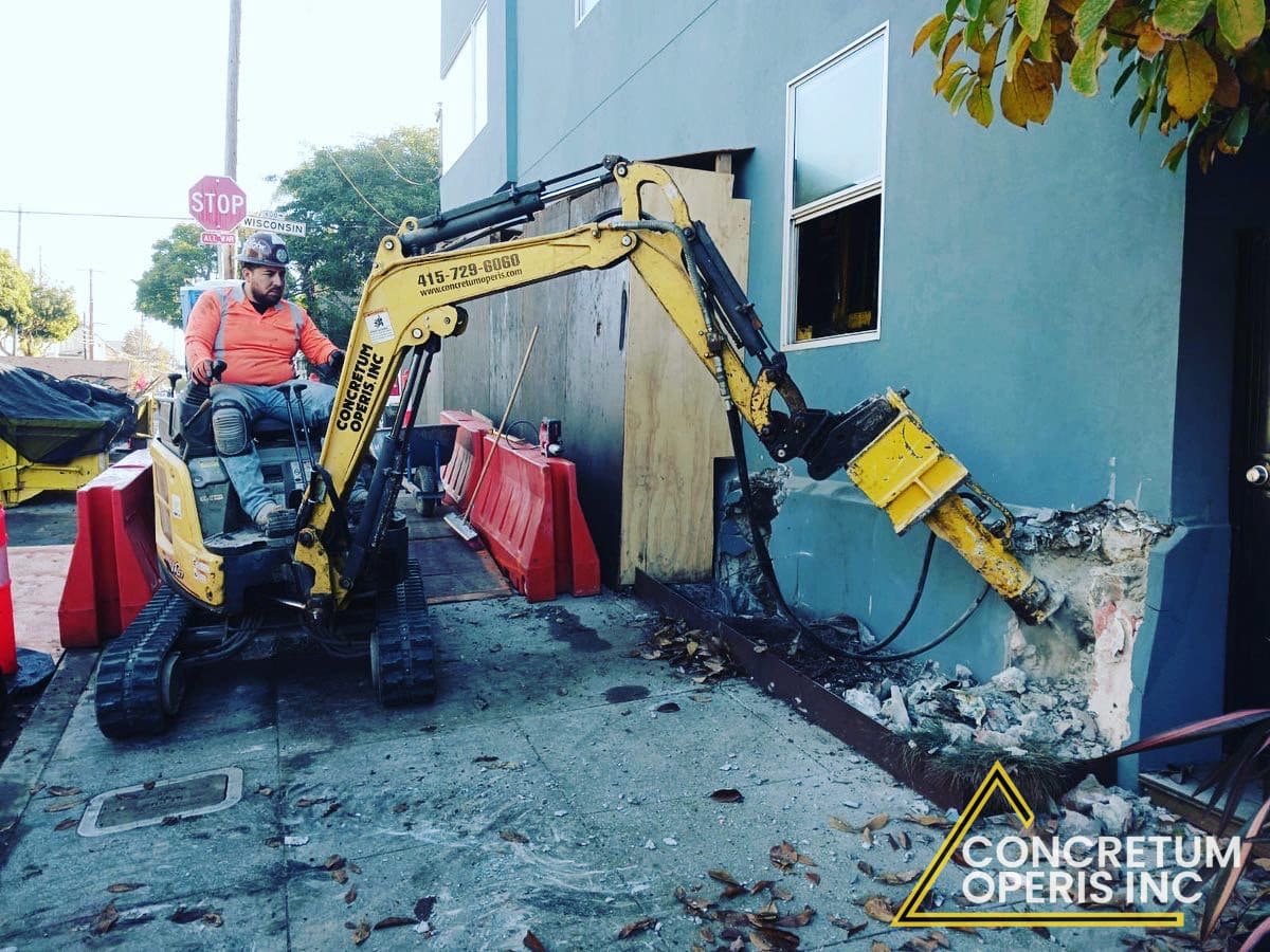 Mini excavator with hydraulic breaker demolishing an exterior wall in Richmond, CA