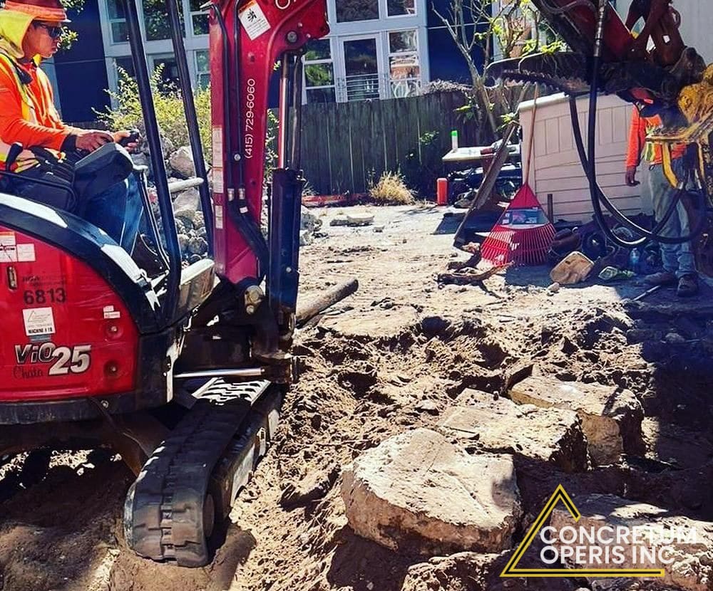 Mini excavator removing broken concrete rubble from a backyard in Richmond, CA