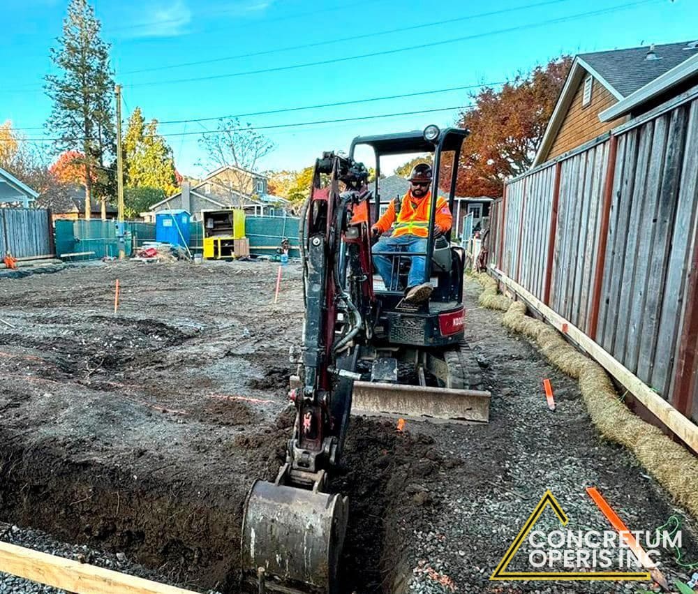Mini excavator digging a trench along a wood fence line in Richmond, CA
