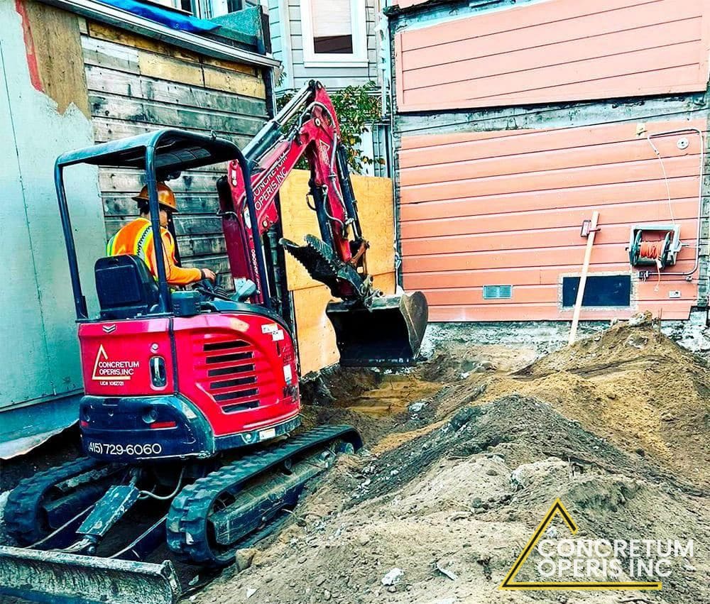Mini excavator digging next to a building in a narrow side yard in Richmond, CA