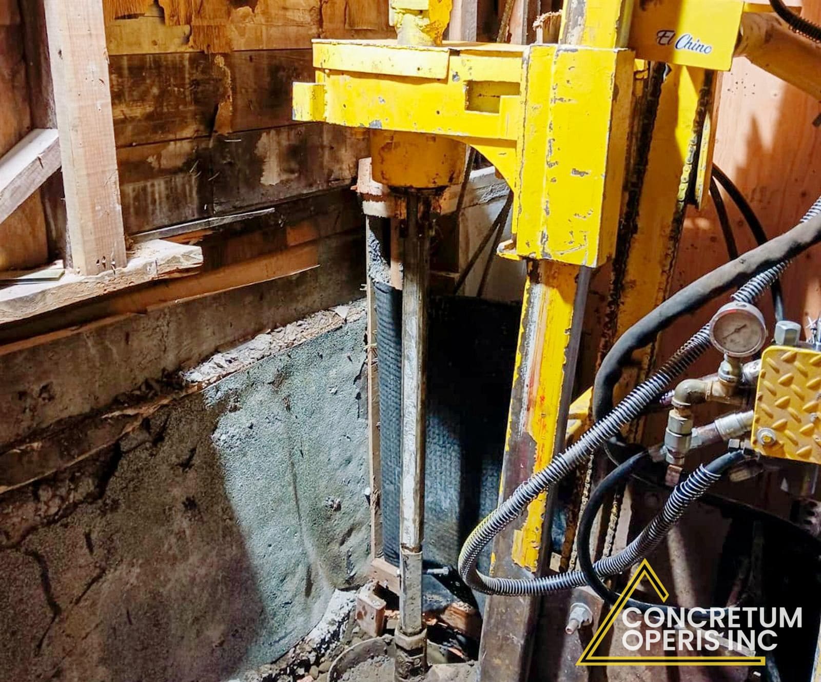 Hydraulic drill rig boring a pier hole along a foundation wall in Richmond, CA
