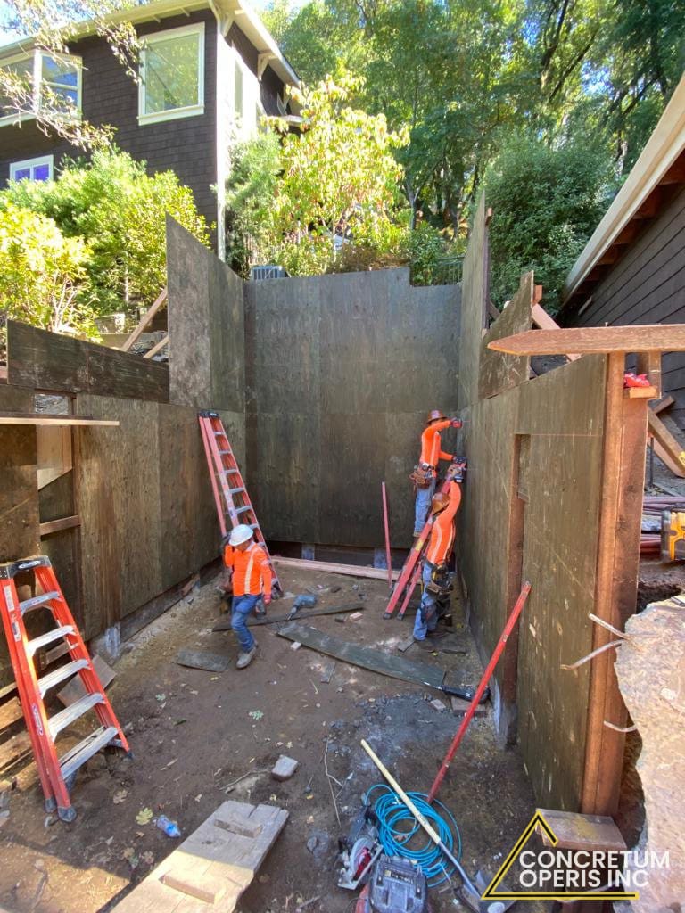 Crew framing plywood forms for a below-grade foundation wall in Richmond, CA