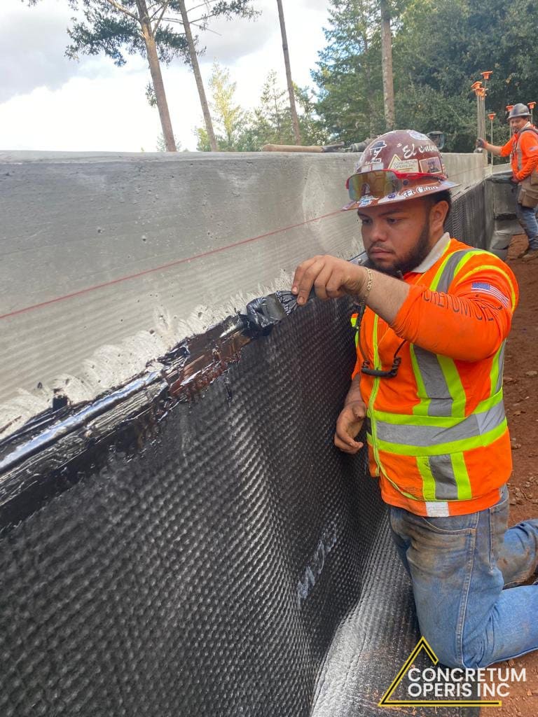 Worker sealing waterproofing membrane seams along a foundation wall in Richmond, CA